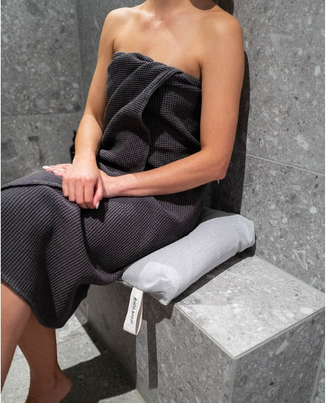 Frau sitzt auf hellgrauem Badesofa Duschkissen in moderner Dusche – komfortables Sitzkissen für Spa-Momente